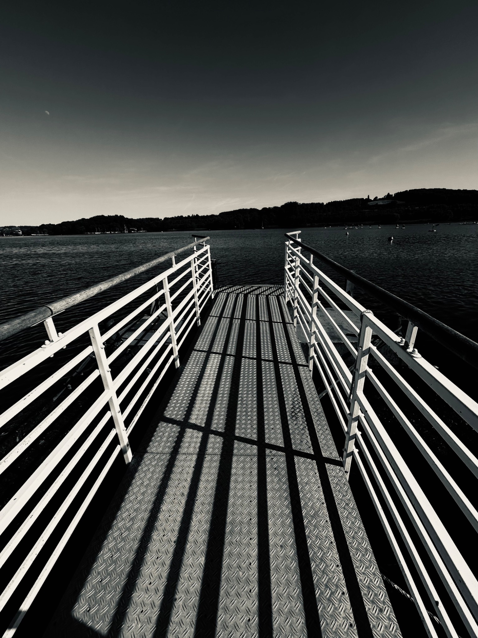 Schwarz-Weiß-Fotografie eines Stegs, der auf einen See hinausführt.